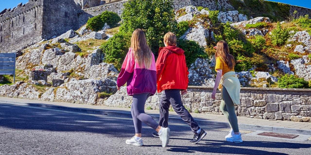three people walking uphill beside stone wall